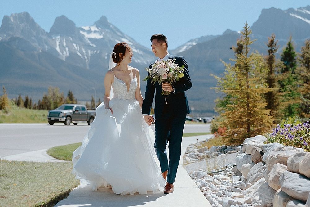 A scenic wedding photo with rocky mountain peaks and spring flowers lining the pathway.
