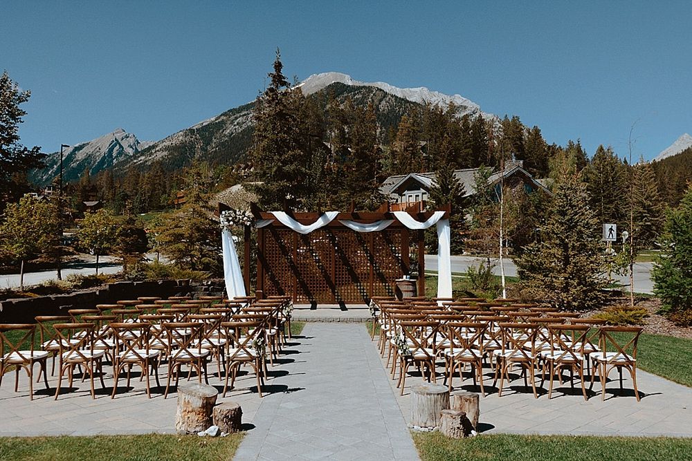 Mountain wedding ceremony setup with wooden chairs and white arch against a stunning alpine backdrop.