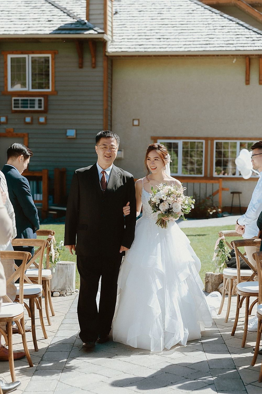 Wedding ceremony aisle lined with wooden chairs leading to a rustic lodge building.