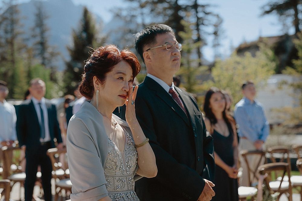 Emotional outdoor wedding ceremony moment with evergreen trees and mountains in background.
