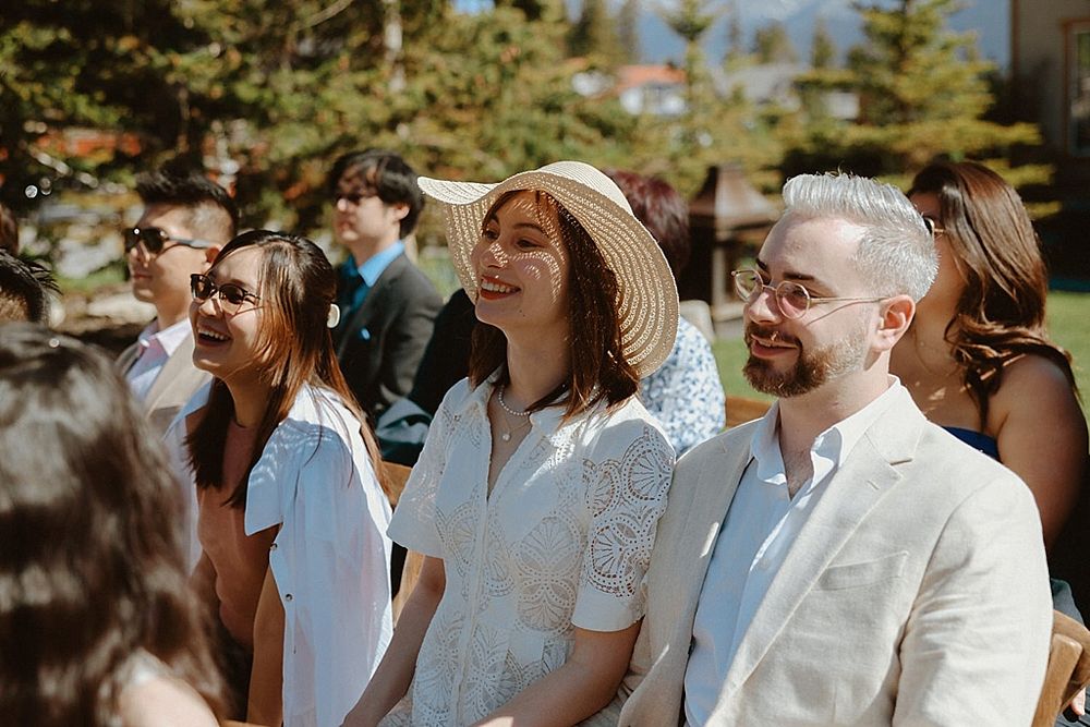 Wedding guests smiling and enjoying outdoor ceremony in sunlit mountain setting.