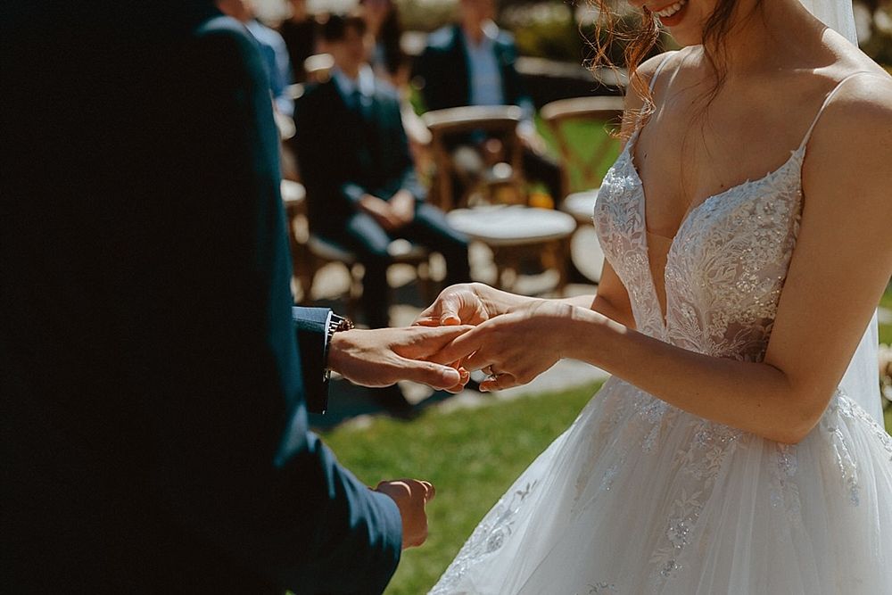 Wedding couple exchanging rings in an intimate outdoor ceremony surrounded by greenery.