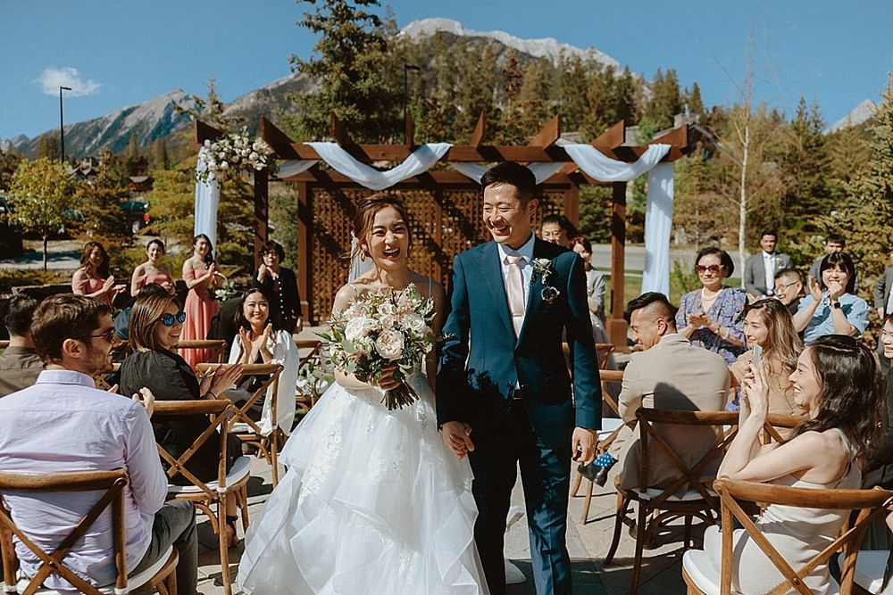Outdoor mountain wedding ceremony with guests seated on wooden chairs.