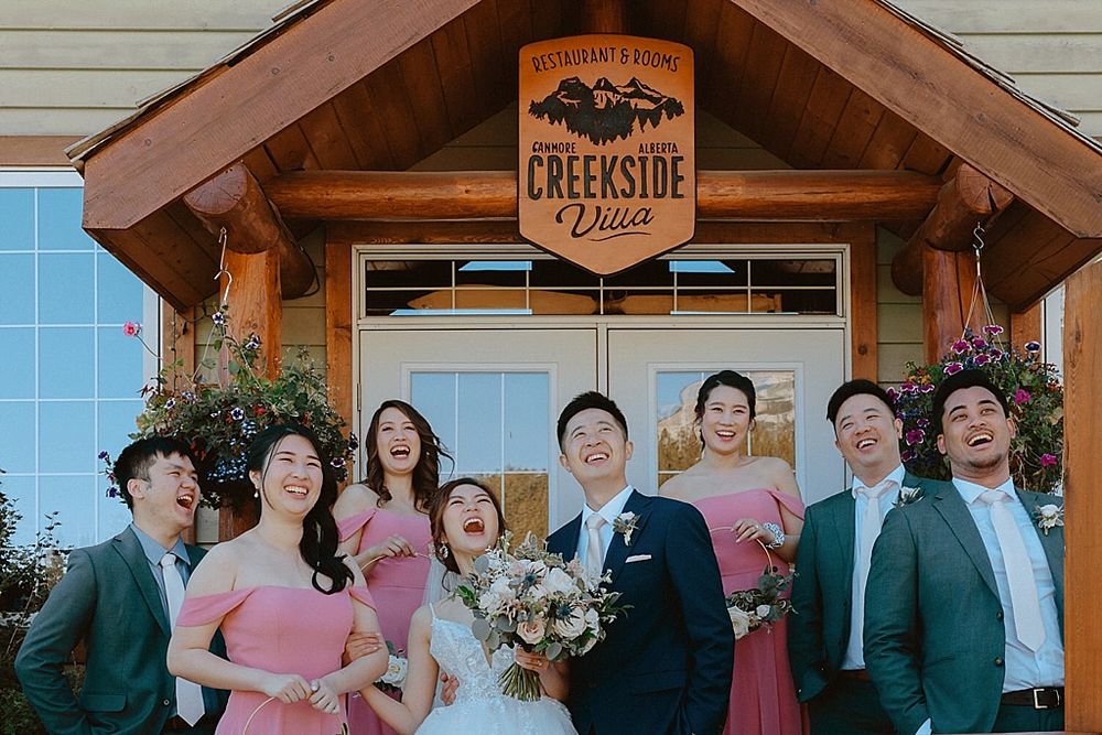 Wedding party posed in front of rustic Creekside venue entrance.