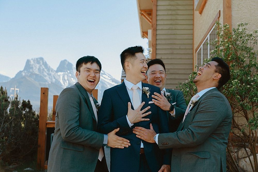 Groomsmen sharing laughter and embracing with mountain peaks in background.