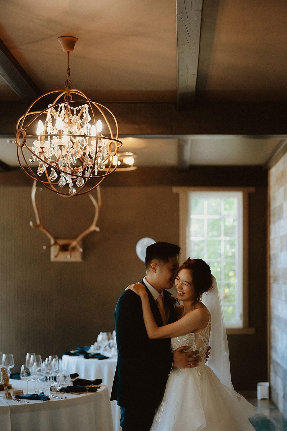 Couple dancing under crystal chandelier in elegant reception room.