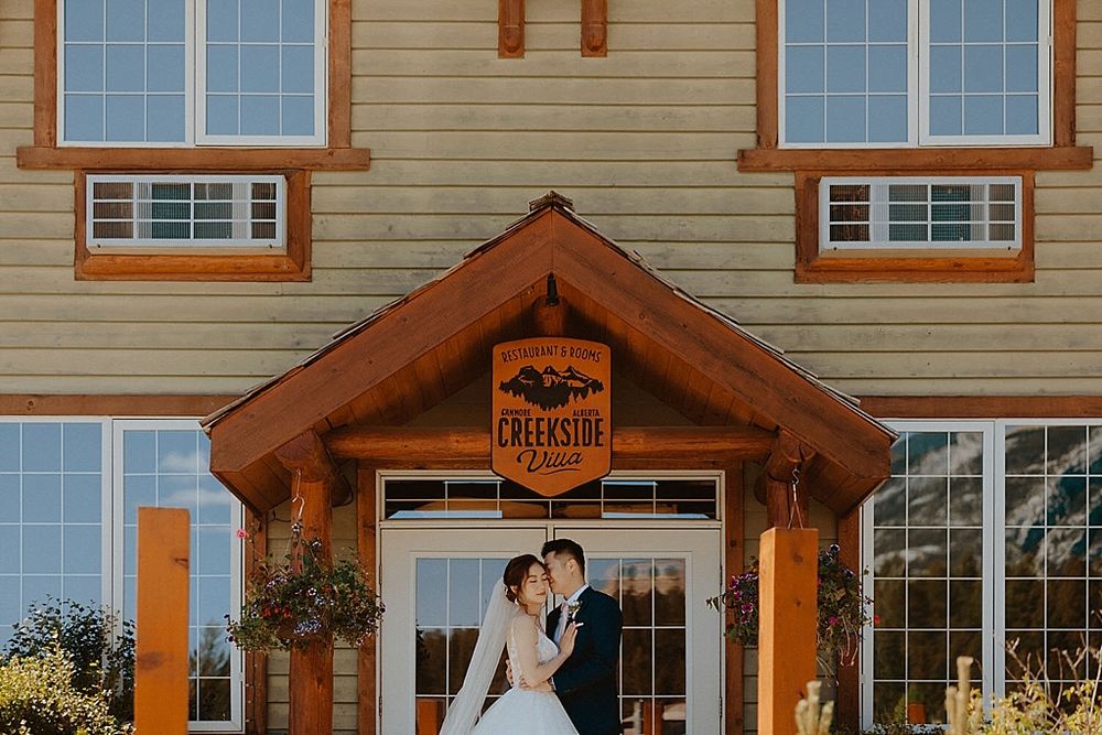 Romantic couple pose at rustic wooden entrance of Creekside venue.