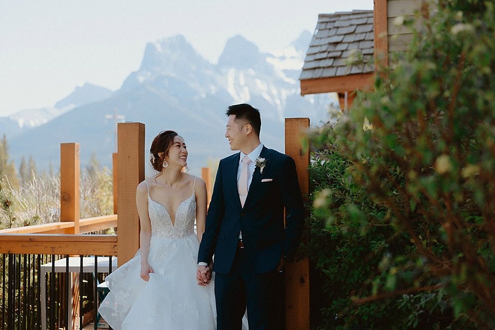 Wedding couple poses against stunning mountain backdrop at rustic wooden lodge venue.