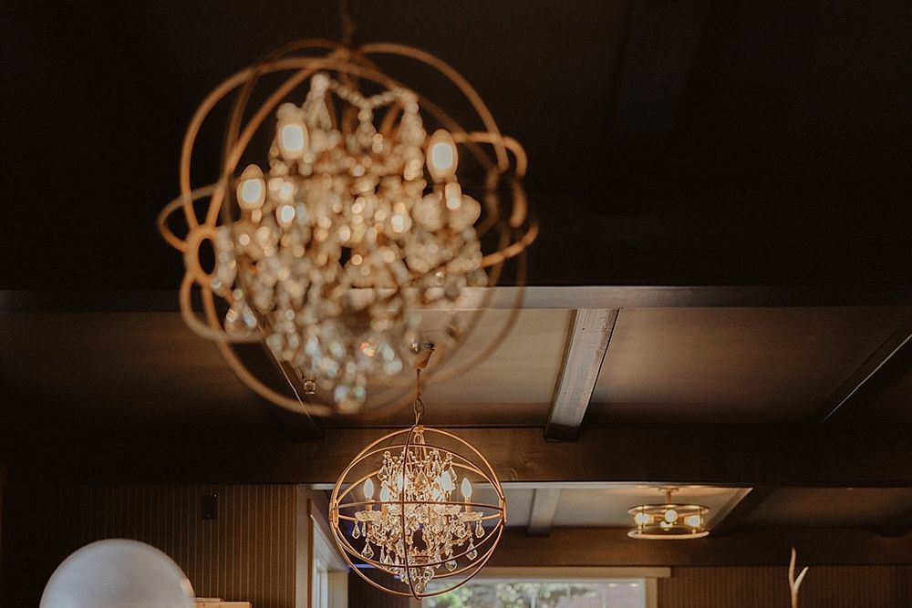 Elegant crystal chandeliers illuminate a rustic indoor venue with exposed wood beams and warm lighting.