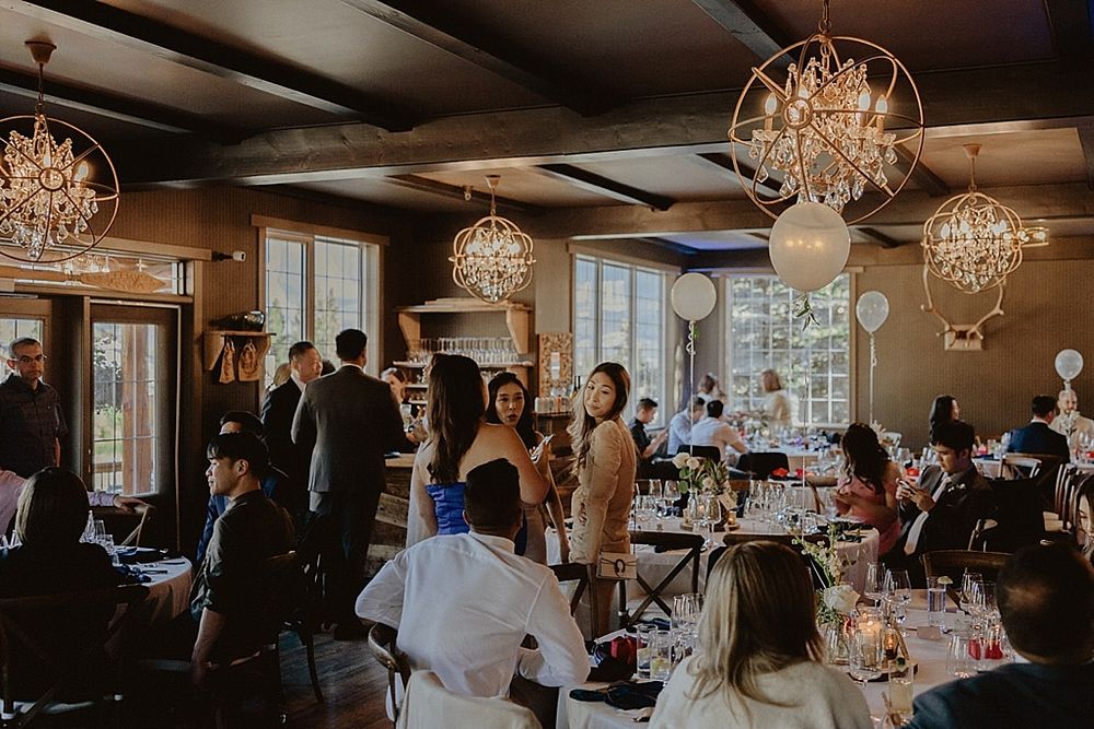 Panoramic view of a wedding reception with elegant table settings and crystal chandeliers overhead.