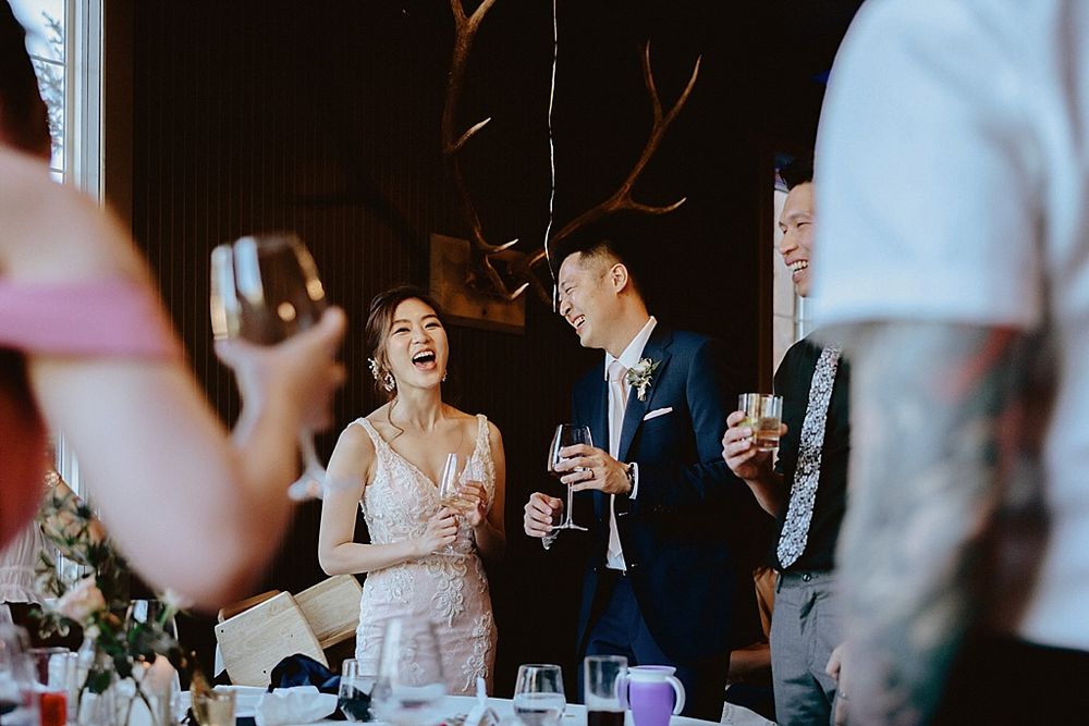 Wedding reception guests celebrating with joyful expressions in an elegantly decorated venue with crystal chandeliers.