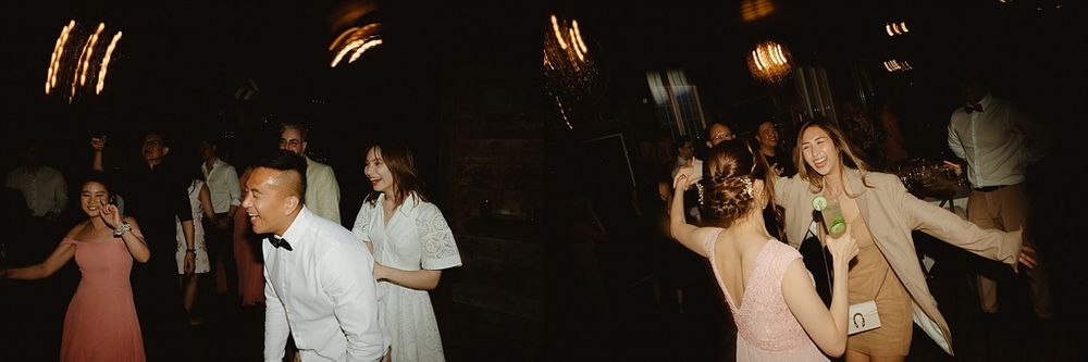 Guests dancing and celebrating at a dimly lit wedding reception with warm lighting overhead.