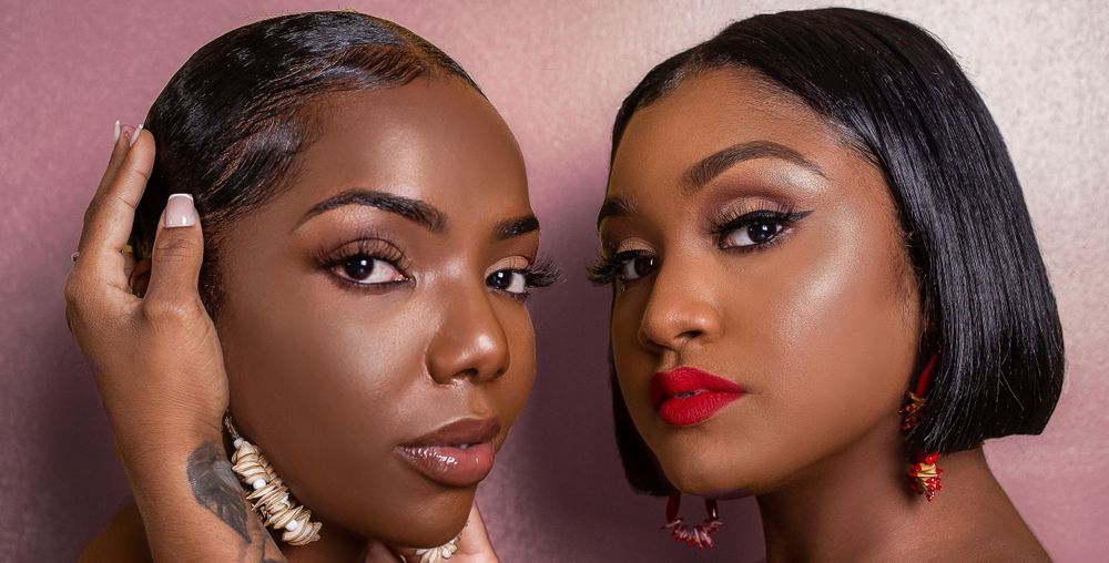 Two Black women with glamorous makeup, one wearing red lipstick, pose together in a beauty shoot.