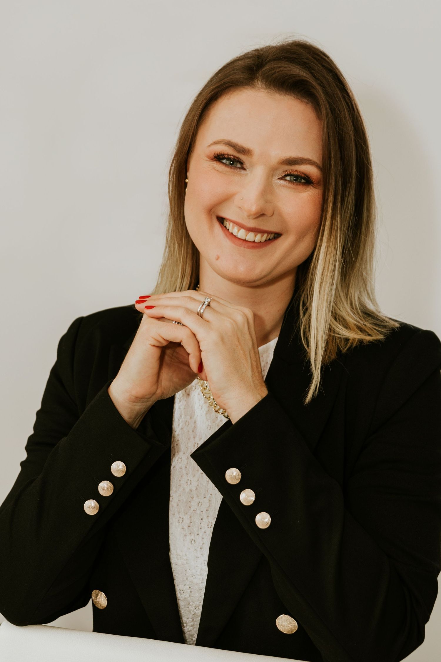 Professional headshot with black blazer, decorative buttons, and confident pose against light background.