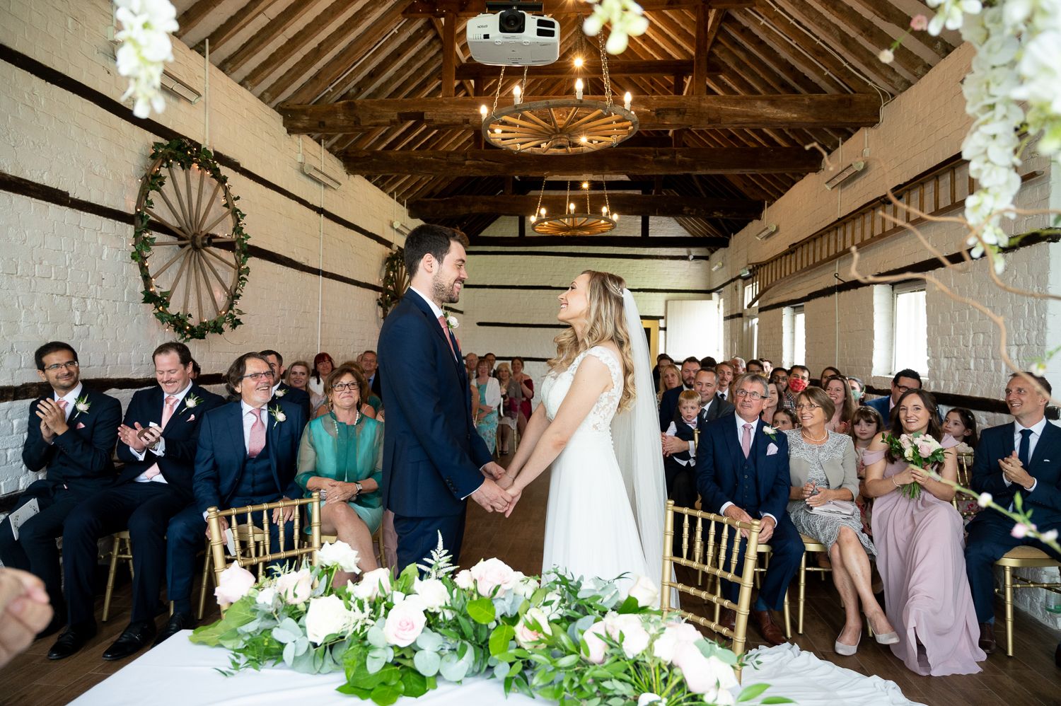 Wedding ceremony in rustic barn venue with guests watching couple exchange vows.