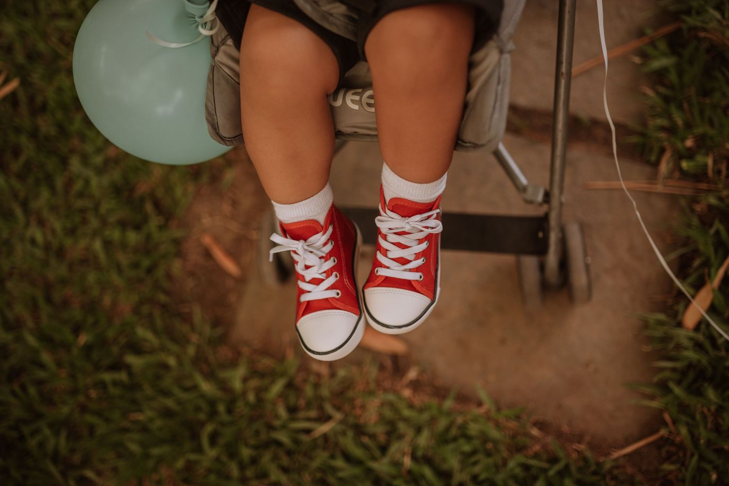 Red converse sneakers on small feet dangling against a grassy background.