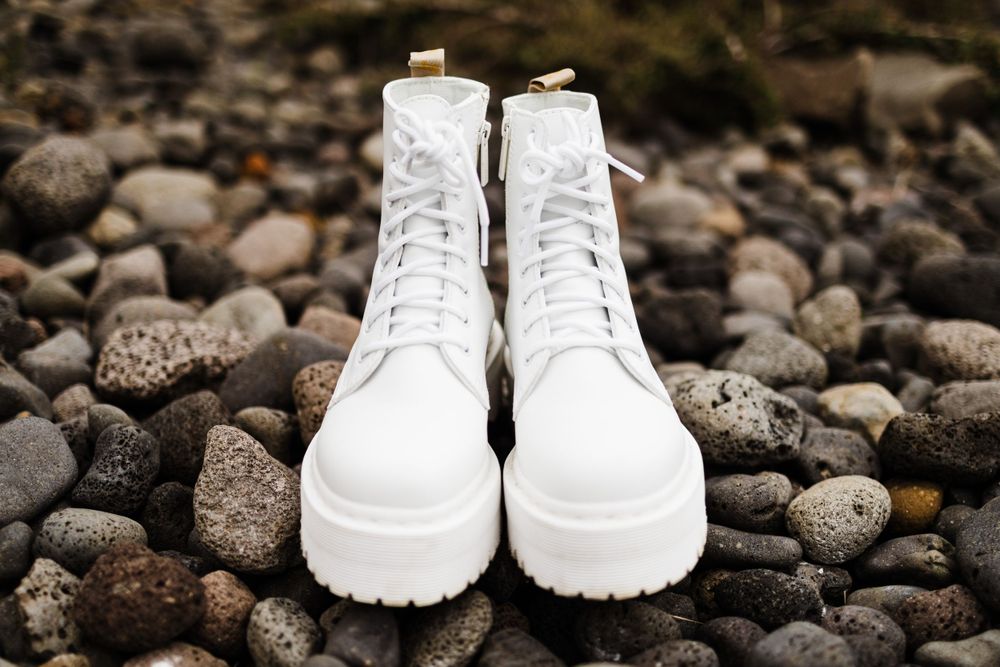 White platform combat boots displayed on rocky terrain with dark stones in the background.