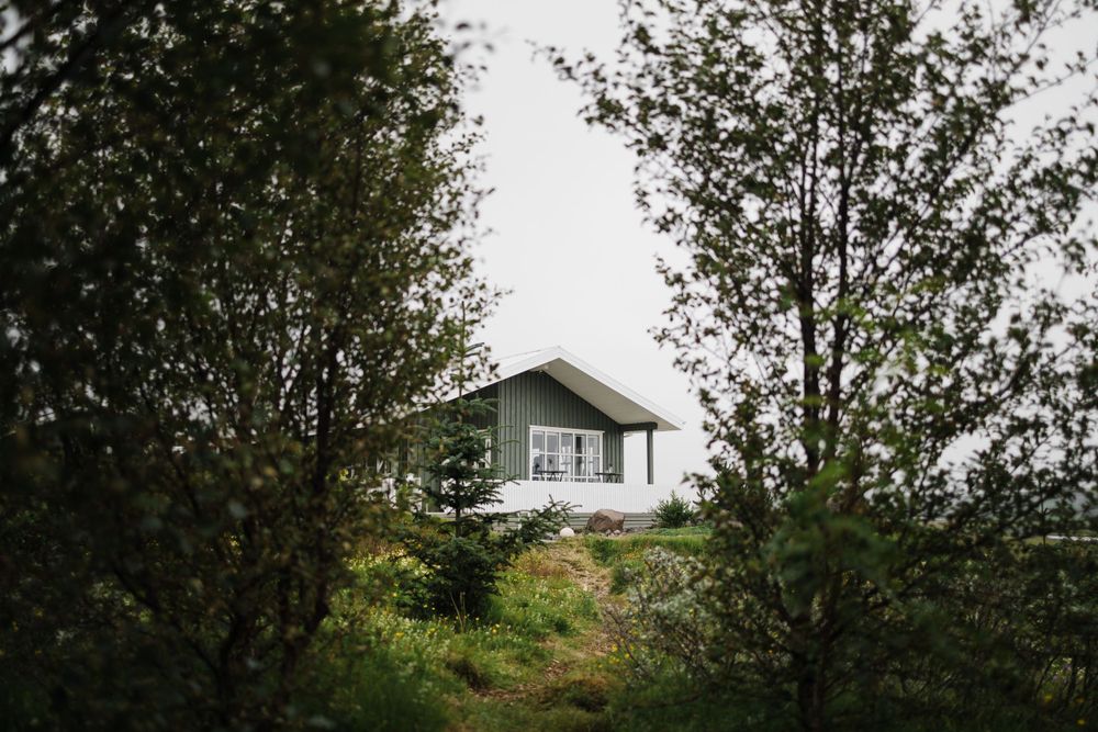 White cottage house nestled among trees viewed from a distance.