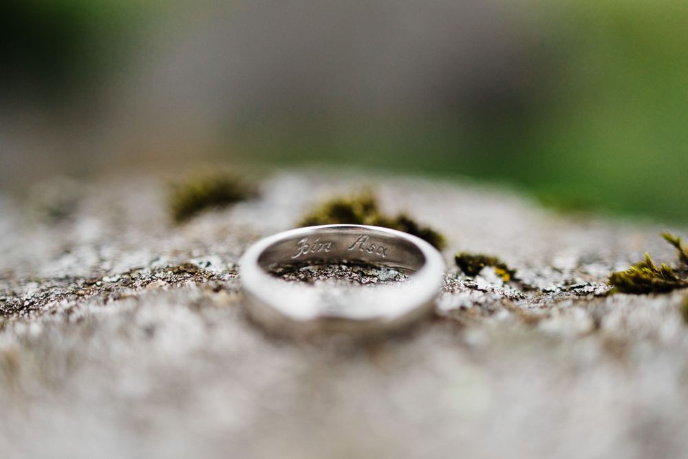 Simple silver wedding band photographed in macro on a textured stone surface.