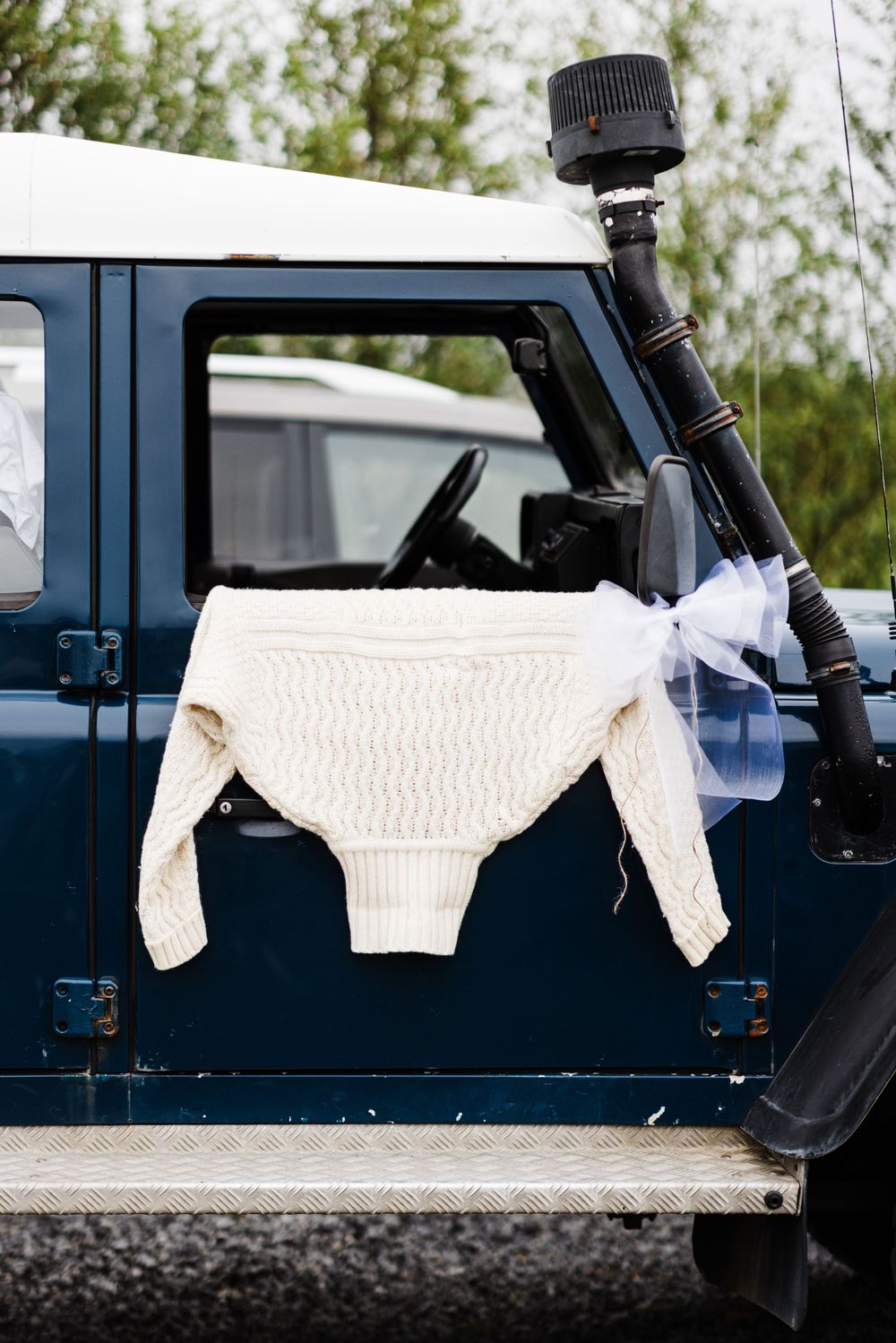 White knit sweater hanging on side of blue vintage off-road vehicle.