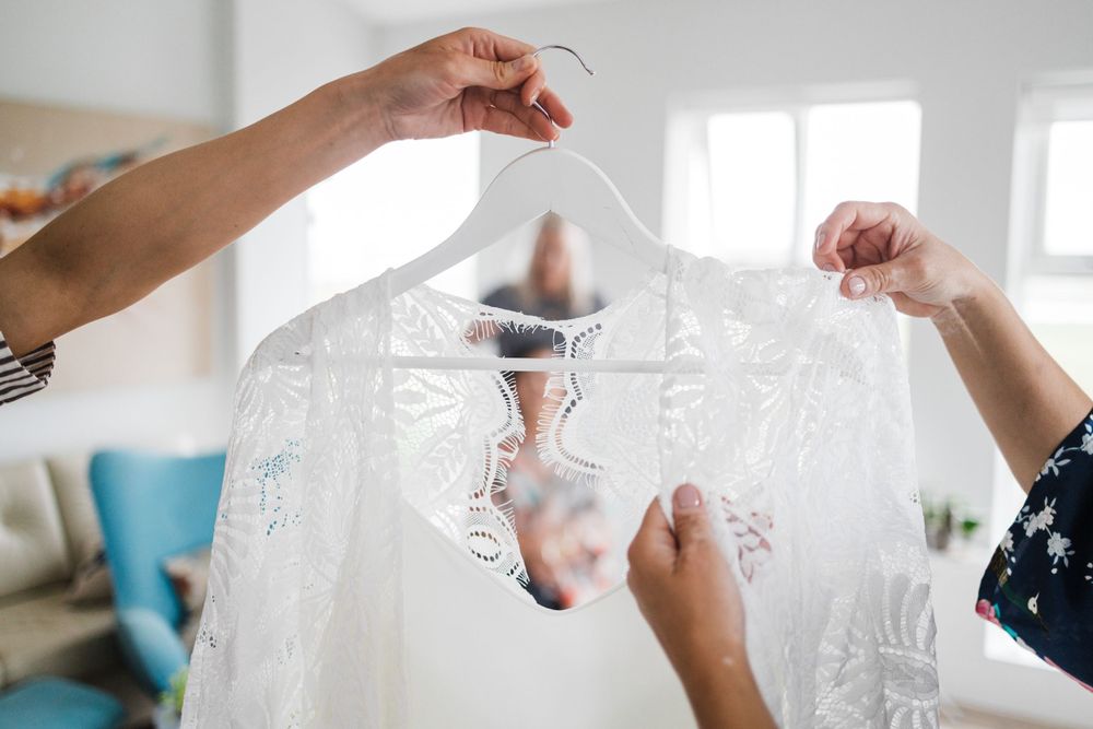 Wedding dress being held up on a hanger in bright indoor setting.