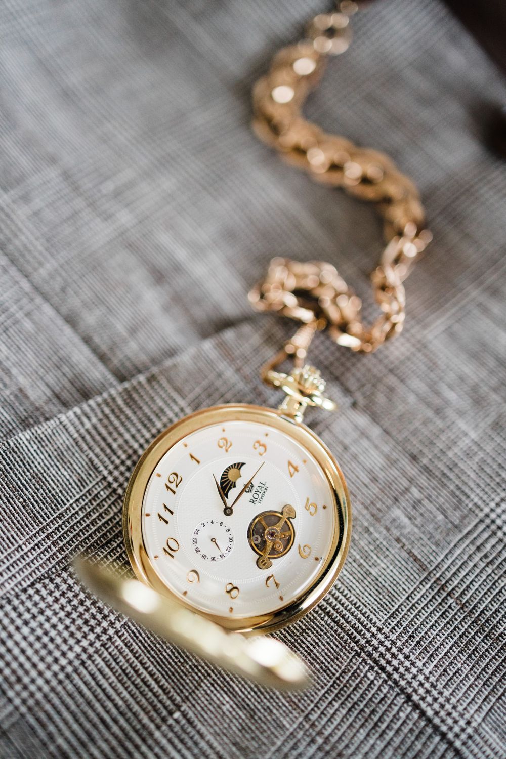 Vintage gold pocket watch with chain lying on grey textile background.