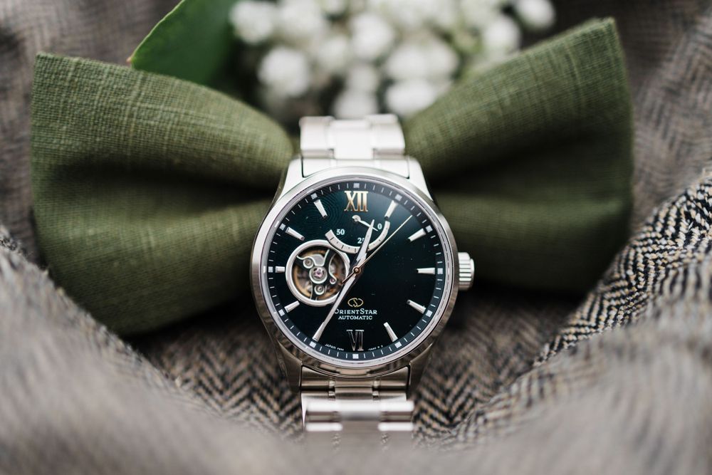 Elegant men's watch with black face displayed against olive green bowtie background.