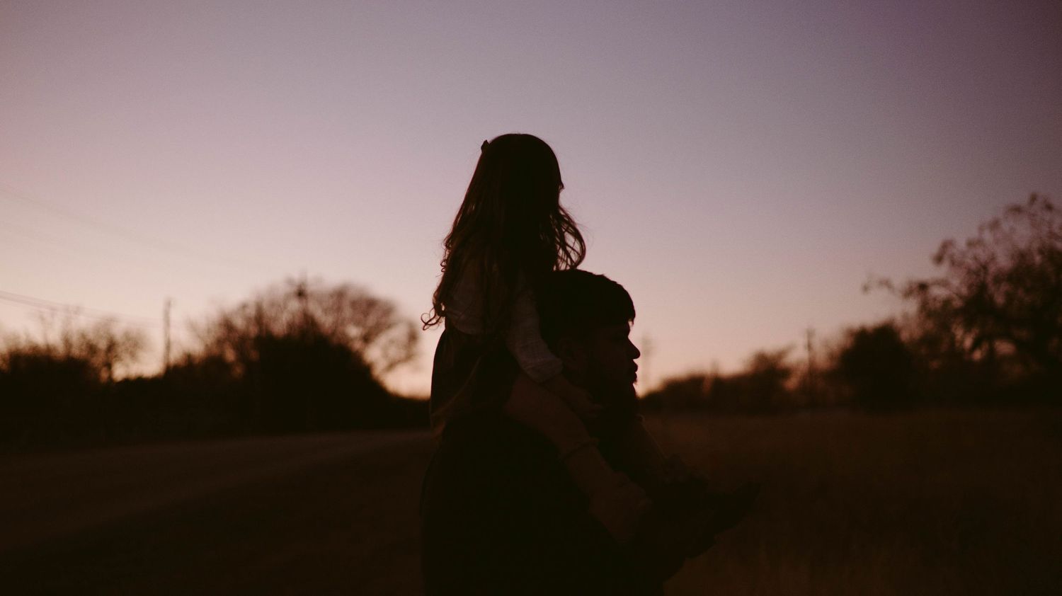 A silhouetted pair against a purple sunset sky in a peaceful field.