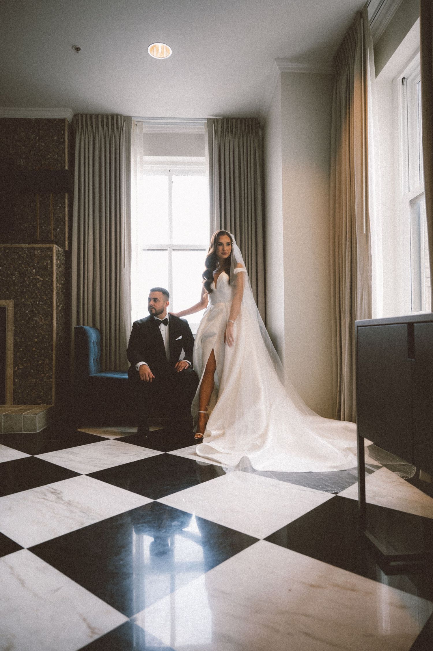 A romantic wedding portrait in a room with checkered floors and flowing curtains.