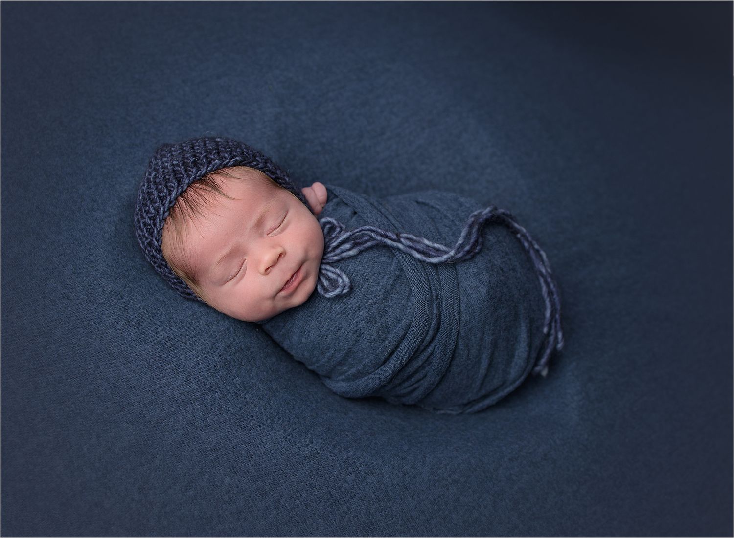 smiling newborn portrait.  baby boy swaddled in blue in a heart.  by Austin Newborn Photographer VAlerie Kay Photography