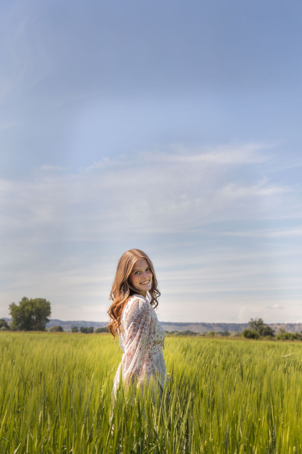 Woman in a white dress stands in a sunlit wheat field at golden hour.