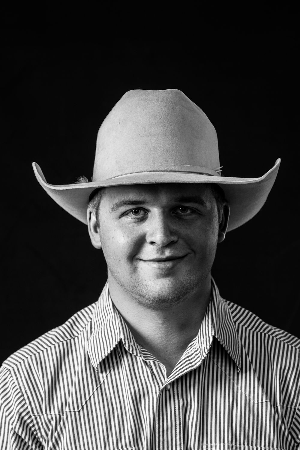 Portrait of person in cowboy hat and striped shirt against black background.