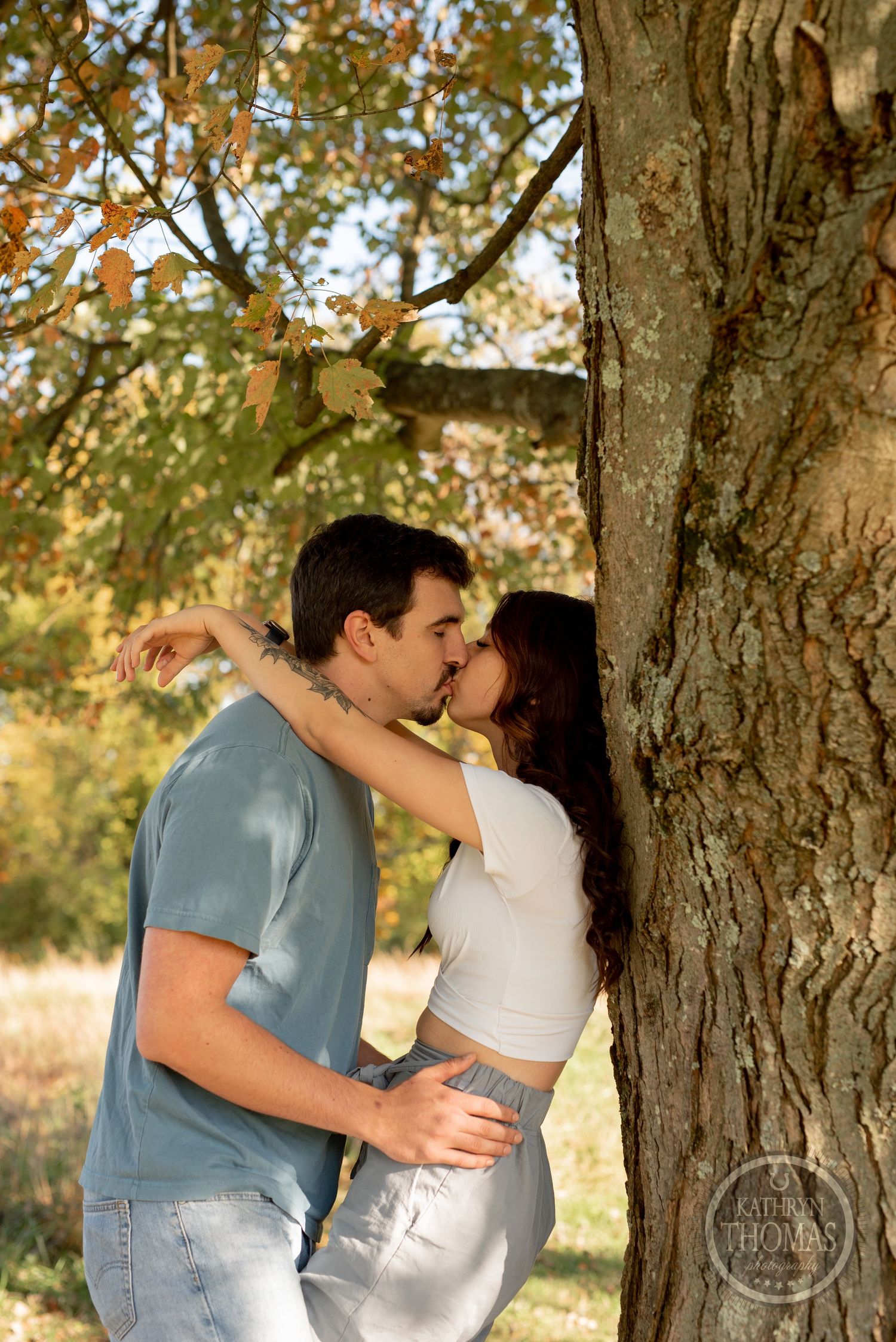 A romantic moment shared between two people near a large tree trunk in warm sunlight.