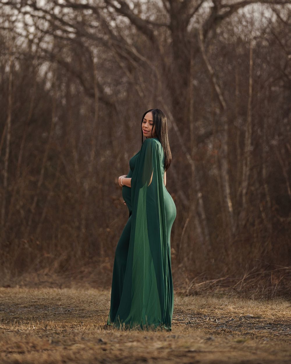 Figure in flowing emerald green dress poses dramatically in winter woodland setting.