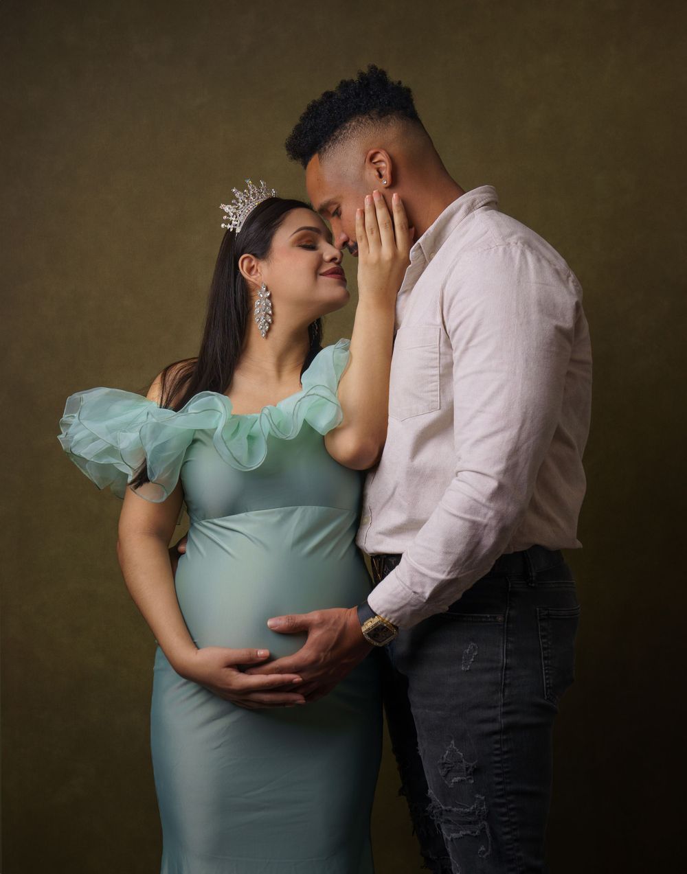 Intimate maternity portrait of couple in blue dress and white shirt against dark backdrop.