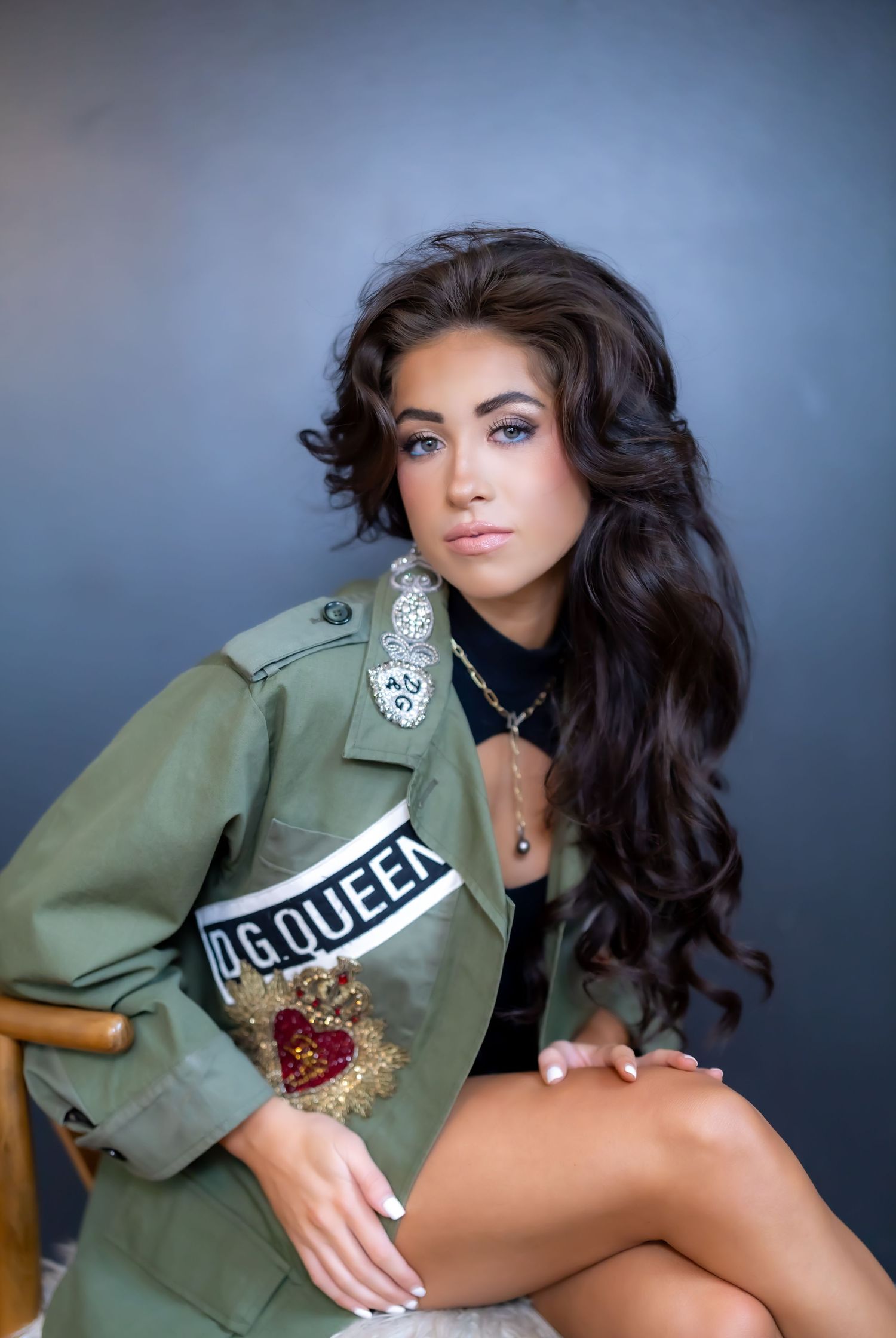 Model in olive military jacket poses against dark background for fashion portrait.