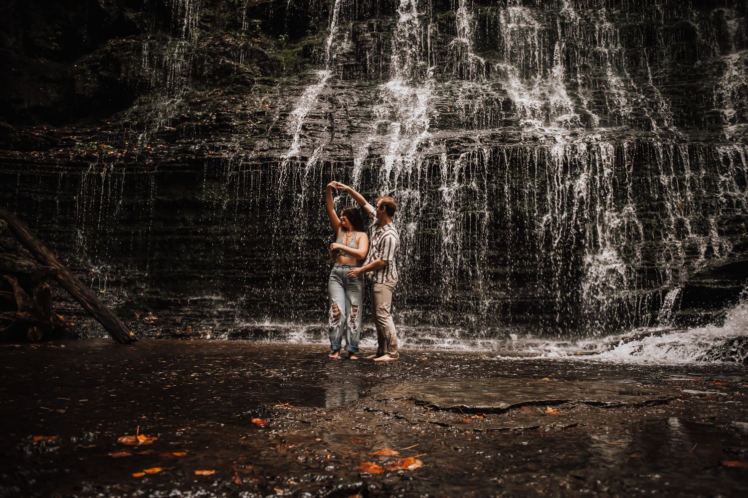 Long exposure of cascading waterfall with autumn leaves in dark moody lighting.