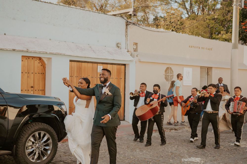 Wedding party celebrates in the street with musicians playing instruments behind them.