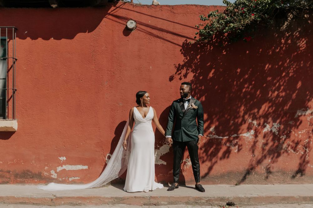 Wedding couple poses against a vibrant coral-colored wall during an outdoor portrait session.