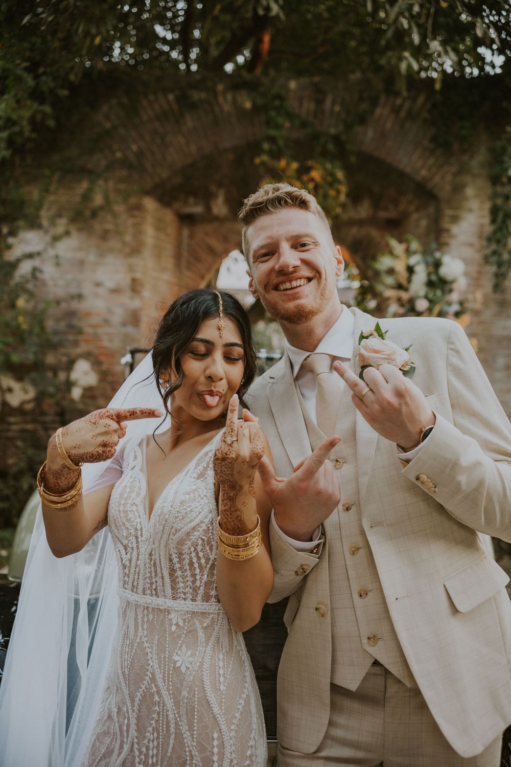 A joyful celebration with a couple showing off their rings against a rustic brick archway backdrop.