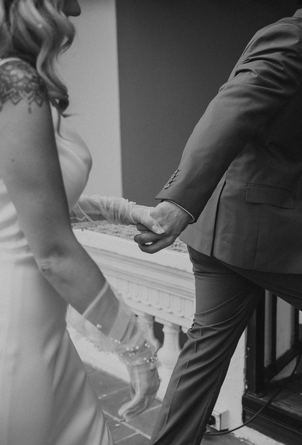 Black and white close-up of a couple holding hands while walking down stairs.