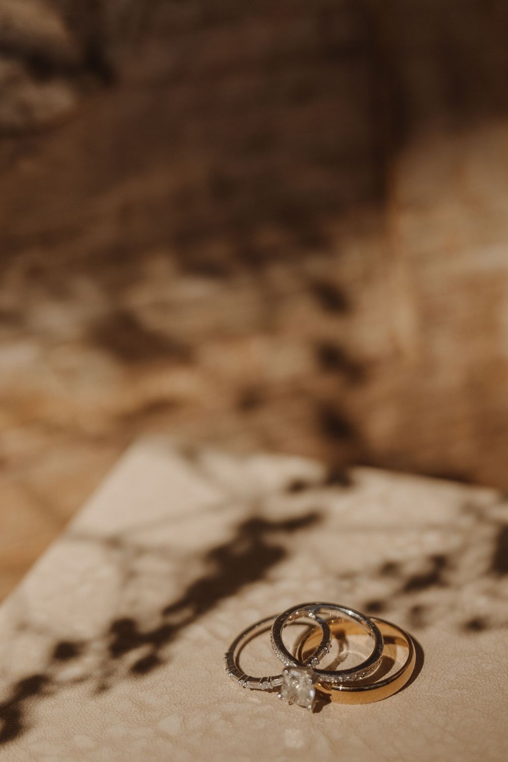 Wedding rings casting dramatic shadows in warm sepia lighting.