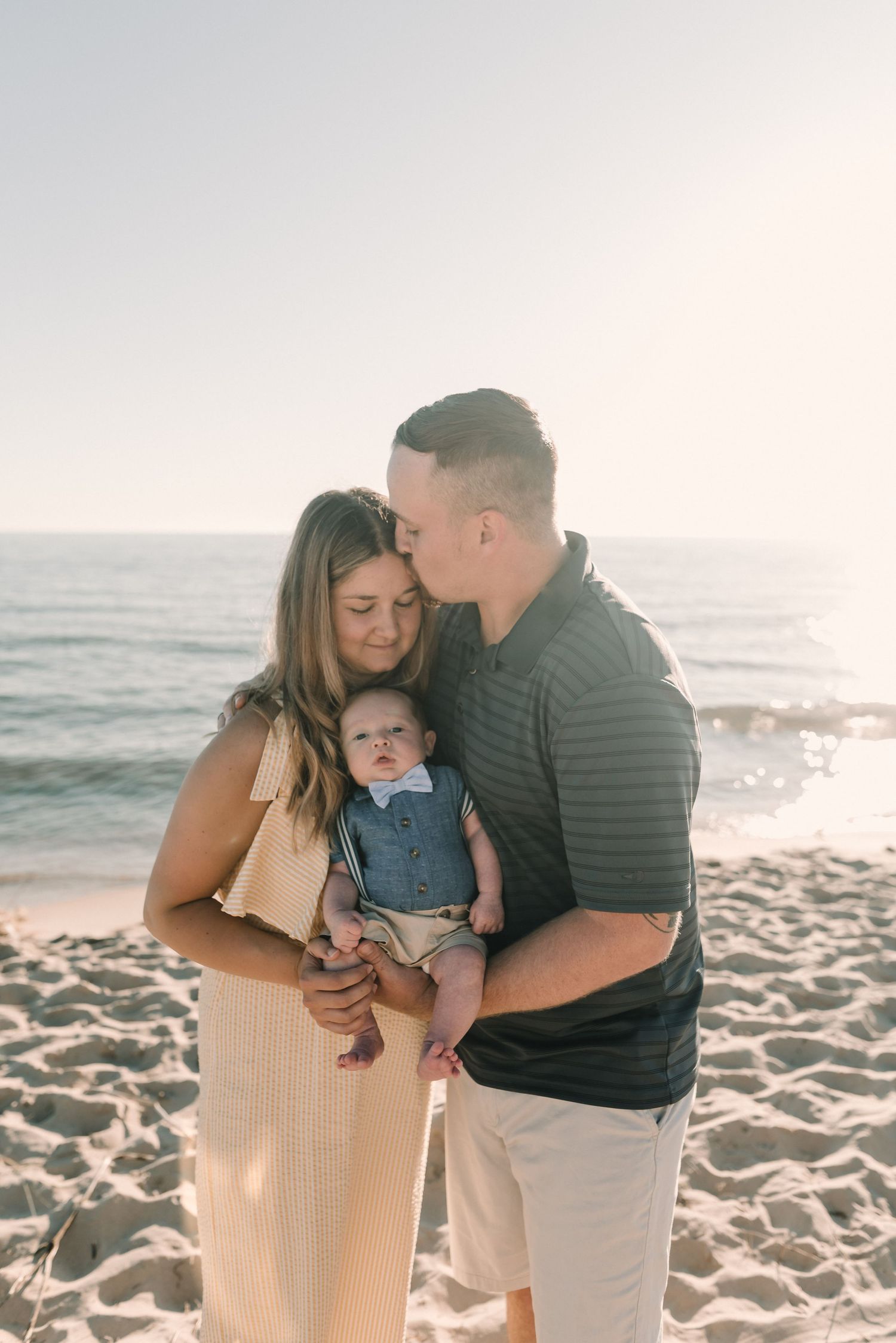 A family shares an intimate moment together on a sunny beach with ocean waves in the background.