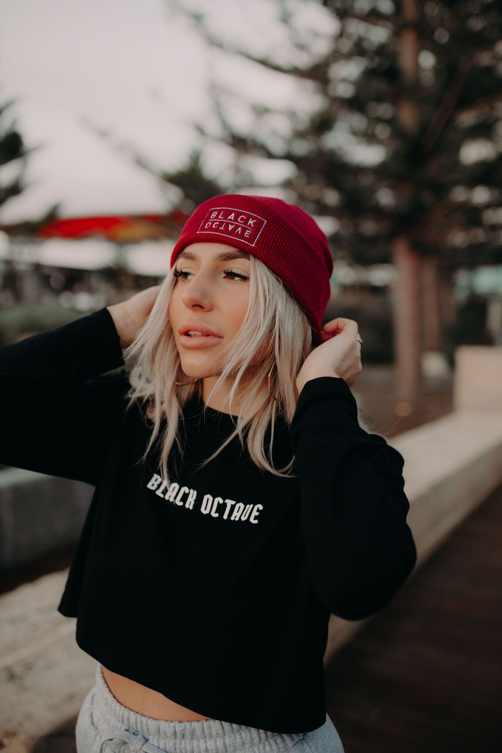 Stylish winter fashion photo featuring a black hoodie and red beanie against a snowy forest backdrop.