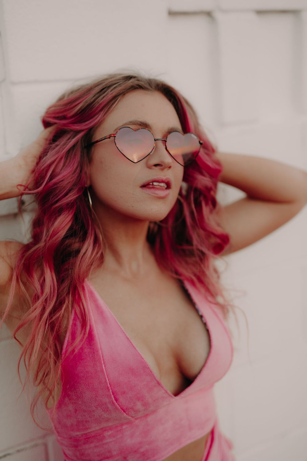 A portrait of someone with vibrant pink hair wearing heart-shaped glasses and pink top.
