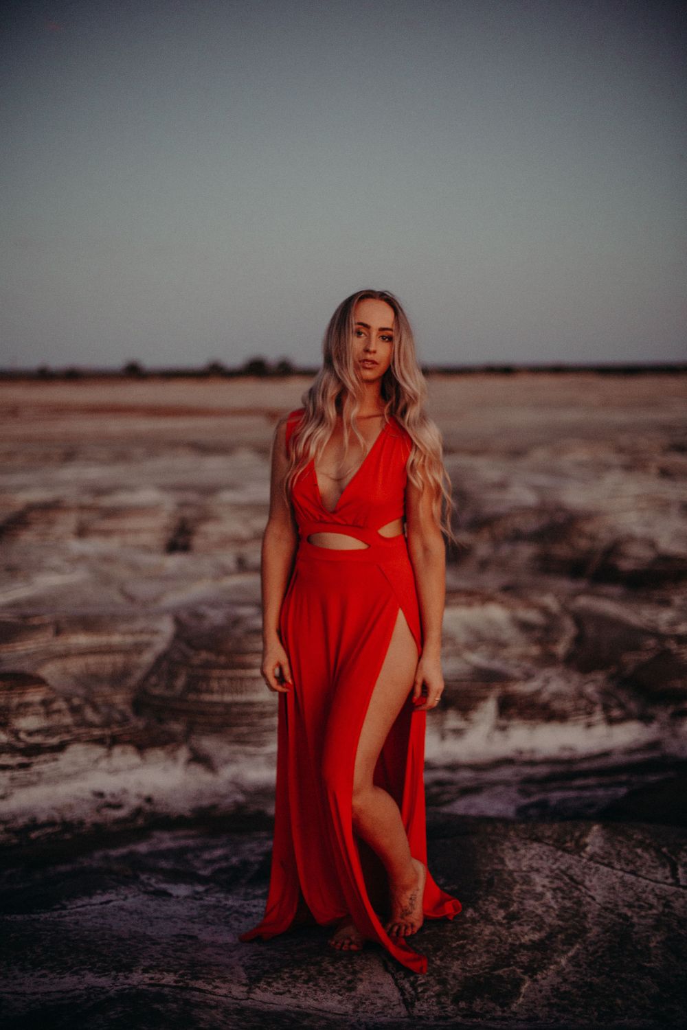 Dramatic desert photoshoot featuring flowing red dress at sunset.