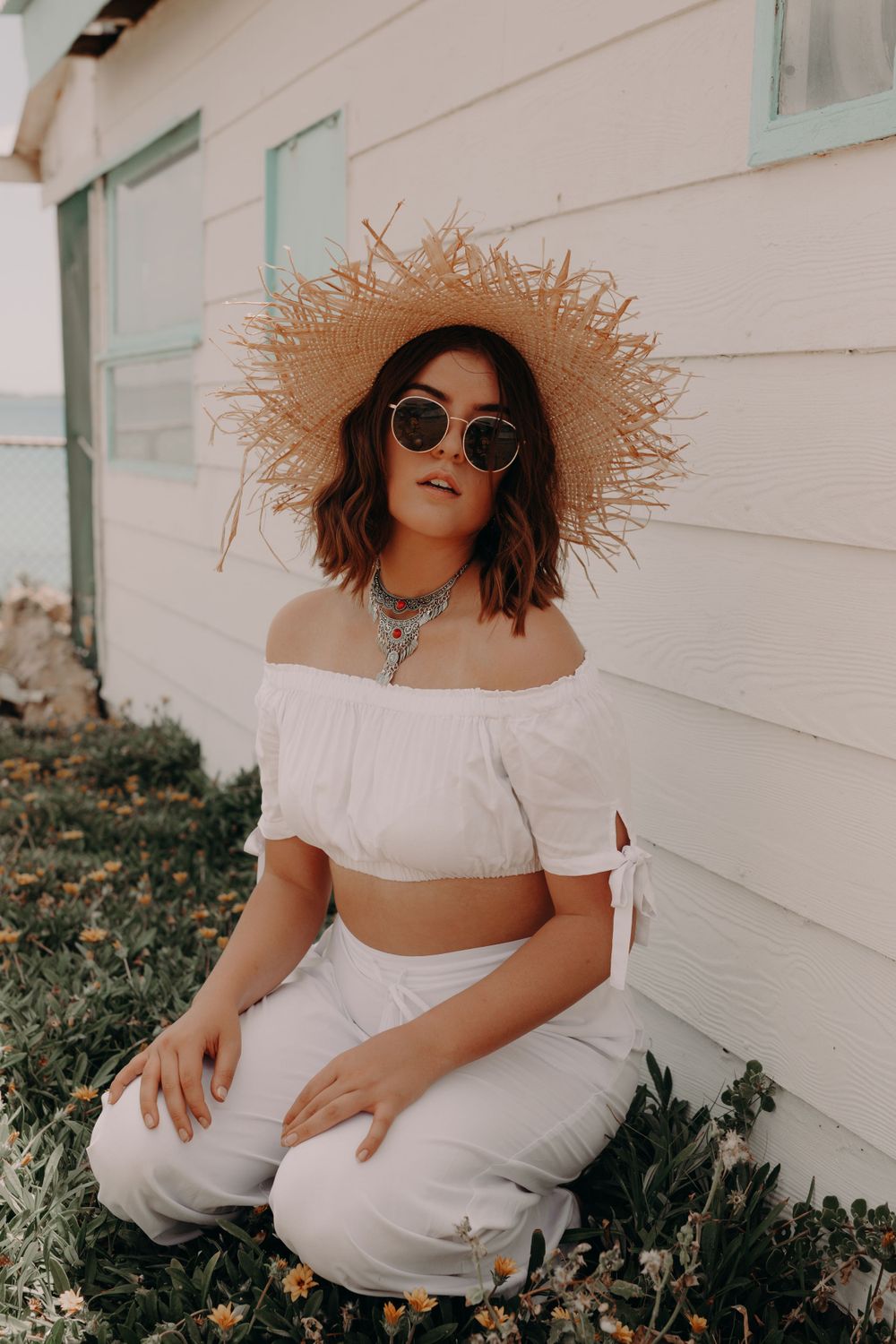 Summer fashion shoot with white outfit and straw hat against white wall.