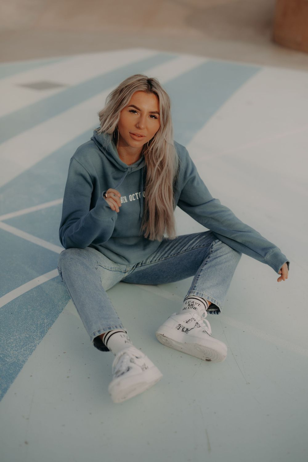 Casual streetwear photography featuring grey sweatshirt and white sneakers on blue floor.
