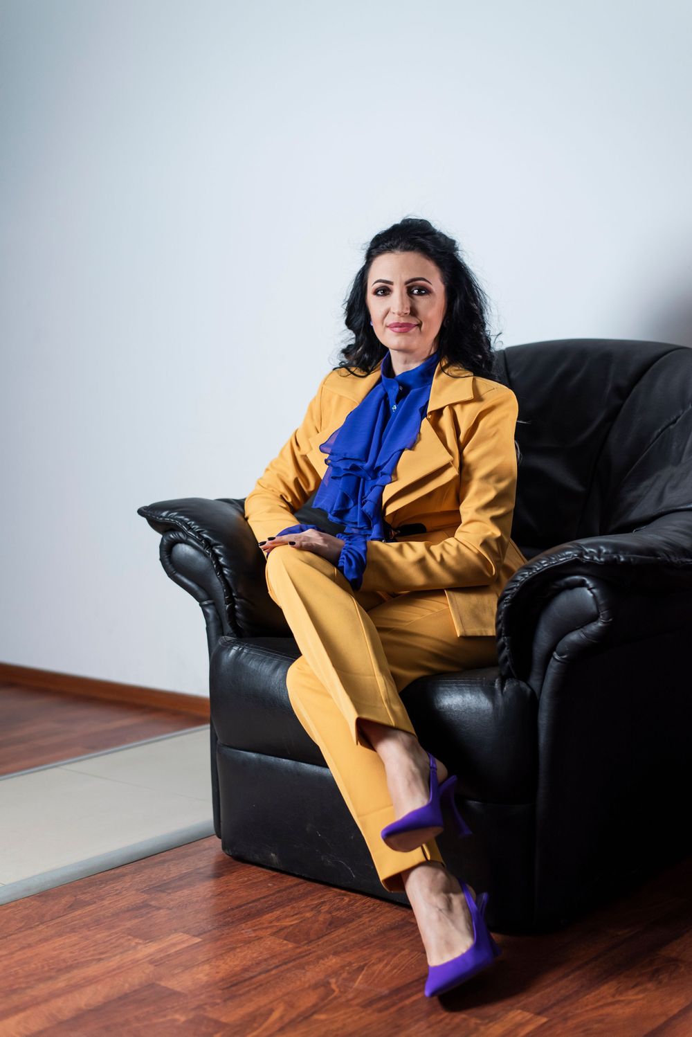 Yellow power suit ensemble paired with blue accessories styled on black leather couch.