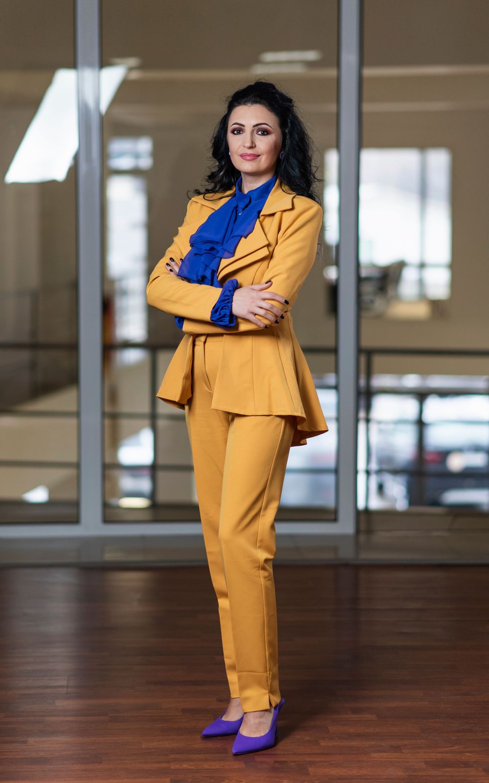 Stylish yellow pantsuit with blue accents photographed in an open office space with hardwood floors.